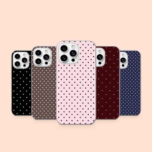 Op de afbeelding: Vijf smartphonehoesjes op een rij, elk met een eigen effen achtergrondkleur zoals zwart, bruin, lichtroze, donkerrood en marineblauw, allemaal versierd met een uniform patroon van kleine witte stippen en uitsparingen voor de camera.