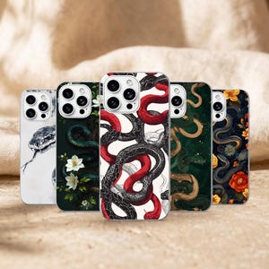 Peut inclure: Cinq coques de smartphone alignées, chacune présentant des illustrations distinctes de serpents et de fleurs. Les motifs incluent une coque blanche avec une tête de serpent, une coque vert foncé avec des fleurs blanches, une coque centrale avec des serpents rouges et noirs, une coque vert foncé avec des serpents dorés et une coque sombre avec des fleurs et des serpents colorés.