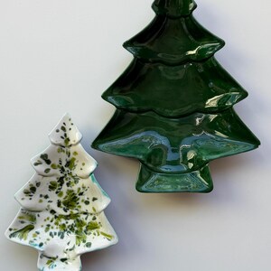 May include: Two ceramic dishes shaped like Christmas trees. One dish is a solid, glossy dark forest green. The second, smaller dish is white with a speckled pattern of green and olive-colored paint splatters across its surface.