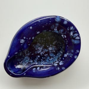 May include: A teardrop-shaped ceramic bowl featuring a deep cobalt blue glaze with a crystalline pattern of white and light blue speckles concentrated around the inner rim and base, creating a textured appearance with a smooth, glossy finish.