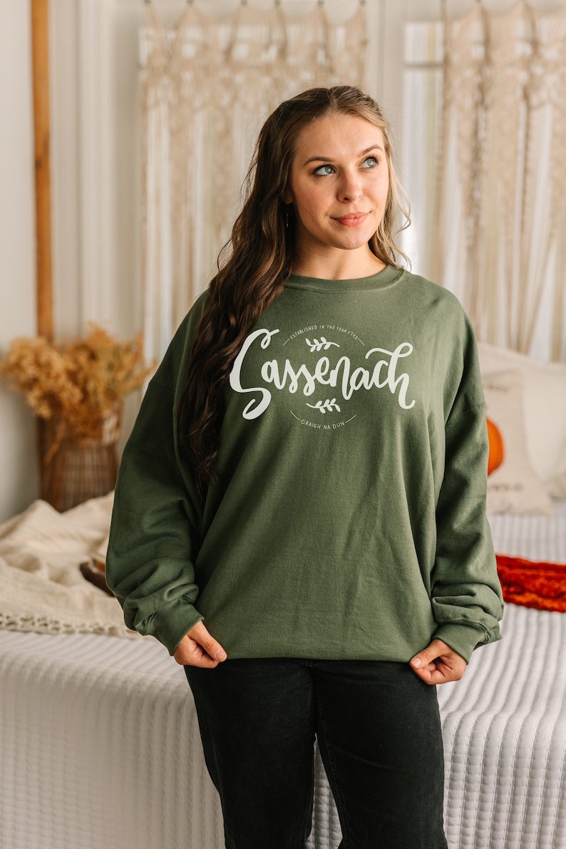 May include: A green sweatshirt with white text that reads "Established in the heart of... Sassenach...  Gracen na Dun".