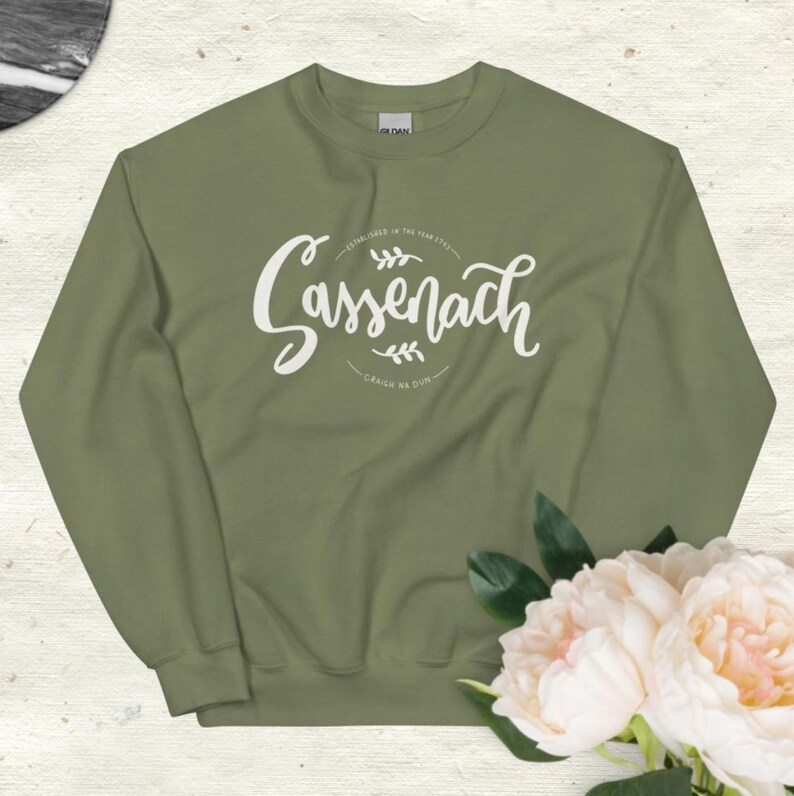 May include: A green sweatshirt with a white graphic print that says "Sassenach" with a floral design and the text "Sassenach is the new style" and "Craig na Dun".
