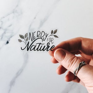 May include: A clear sticker with the text "Nerdy for Nature" in black script with green leaf illustrations.