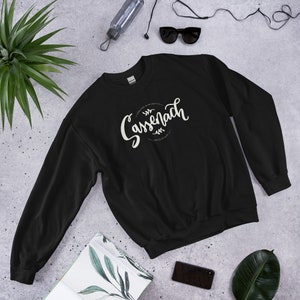 Black crew neck sweatshirt with hand lettered design that reads Sassenach , established in the year 1743, Craigh na Dun and shows two laurels above and below the lettering.