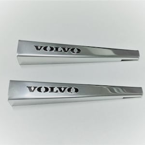 以下が含まれることがあります： 黒い大文字でVOLVOという単語が印刷された、銀色のくさび形の金属製トリムピース2点。これらの細長く先細りになったコンポーネントは、滑らかで反射性のある仕上げと、独特の角張ったプロファイルが特徴です。