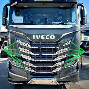 Peut inclure: Vue frontale d'un camion Iveco S-Way gris foncé avec une calandre chromée à motif nid d'abeille, de grands phares et des rétroviseurs latéraux. Le mot IVECO est centré en lettres chromées au-dessus de la calandre, avec des lignes vertes soulignant le design.