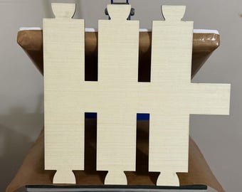 May include: A light-colored, unfinished wooden cutout featuring a geometric shape with three vertical rectangular sections, each topped and bottomed with a small semi-circular tab, and an additional horizontal rectangular extension on the right side.