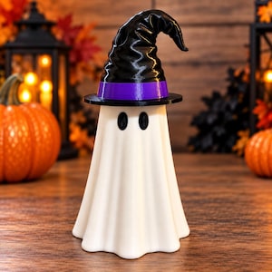 May include: A white ghost figurine wearing a black witch hat with a purple band. The ghost has a smooth, draped body shape with two oval black eyes. The hat features a pointed, slightly curved top and a wide brim, sitting atop the ghost's head.