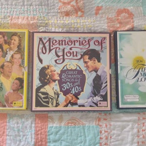 Op de afbeelding: Drie vintage vinyl platen met kleurrijke hoezen. De eerste plaat is geel en toont een groep mensen die lachen. De titel is "I've Heard That Song Before". De tweede plaat is bruin en toont een stel in een romantische omhelzing. De titel is "Memories of You" met de tekst "Great Romantic Songs 30s and 40s". De derde plaat is zwart en toont een witte madeliefje met de tekst "Fifty Years of Music America Loves Best" en nummers die decennia van de jaren 30 tot de jaren 80 voorstellen.