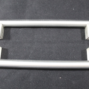 May include: Two silver cabinet door handles with a square shape at each end. The handles are made of metal and have a brushed finish.