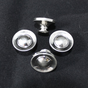 May include: Four silver-toned cabinet knobs with a rounded, domed center and a decorative base. One knob is upright, while the other three are face-up, showcasing their reflective surfaces. The knobs are arranged on a dark background.