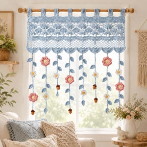 May include: A light blue crochet window valance featuring a scalloped top edge and a lattice pattern. Hanging from the bottom are multiple vertical strands decorated with crocheted pink flowers, white flowers, blue leaves, and small brown acorns.