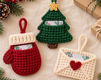 May include: Three crocheted ornaments with hanging loops, designed as a red mitten with a cream cuff, a green Christmas tree with a yellow star, and a cream envelope with a red heart, each containing a small card with a botanical print.
