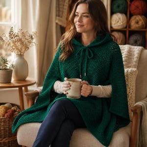 Puede incluir: Un poncho con capucha de color verde oscuro que presenta un patrón de punto texturizado, un cuello con cordón ajustable con herretes plateados y un diseño abierto. La prenda se lleva sobre una camisa beige de manga larga y pantalones vaqueros azul oscuro.