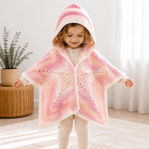 May include: A hooded crochet poncho featuring a star-shaped design in a gradient of soft pink, cream, and white yarn. The garment has an open front, long sleeves, and a pointed hood, crafted with a textured stitch pattern throughout the fabric.