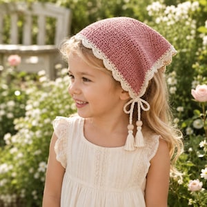 May include: A dusty rose triangular headscarf crafted from crochet fabric, featuring a delicate cream-coloured scalloped lace border. The headscarf includes two long cream-coloured ties adorned with wooden beads and matching cream-coloured tassels.