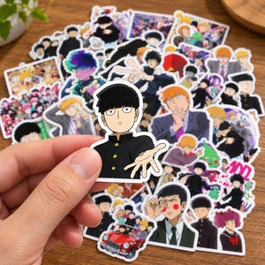 Puede incluir: Una colección de pegatinas de vinilo con varios personajes de anime de Mob Psycho 100, incluyendo una pegatina central troquelada de un chico con corte de pelo estilo tazón negro y uniforme negro, con otras pegatinas que muestran diversas escenas.