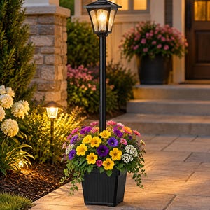 May include: A black square planter base with a tall central post supporting a four-sided lantern light fixture. The planter is filled with a vibrant arrangement of yellow, purple, pink, and white flowers with green foliage, creating a bright display.