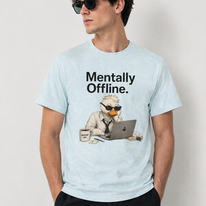 Op de afbeelding: Een lichtblauw gemêleerd T-shirt met een afbeelding van een eend met een zonnebril, een wit overhemd en een stropdas, zittend achter een laptop. De tekst "Mentally Offline." staat boven de eend en er staat een koffiemok naast.