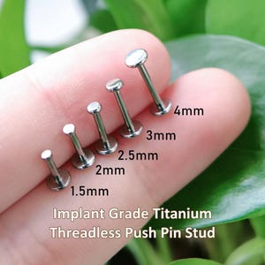 Może przedstawiać: Pięć srebrnych, bezgwintowych kolczyków typu push-pin z tytanu medycznego o różnych długościach, oznaczonych jako 1,5 mm, 2 mm, 2,5 mm, 3 mm i 4 mm. Każdy kolczyk ma płaską, okrągłą główkę i płaską podstawę, ułożone w rzędzie według rozmiaru.