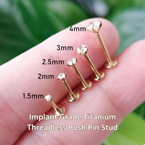 May include: Five gold-colored implant grade titanium threadless push pin studs with clear stones, ranging in size from 1.5mm to 4mm. Each stud features a flat back and a prong-set stone, with the specific size labeled next to each individual piece.
