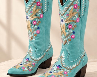 May include: A pair of turquoise mid-calf boots featuring intricate floral embroidery in shades of pink, white, and tan, accented with small metallic studs. The boots have a pointed toe, a stacked block heel, and pull tabs at the top openings.
