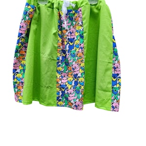 May include: A green skirt with a tie at the waist. The skirt has colorful bear print panels on the sides.