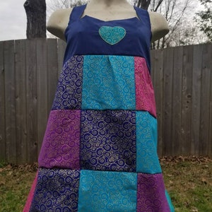 May include: A blue and multi-colored patchwork dress with a heart-shaped design on the bodice. The dress has a square patchwork pattern with swirls on each square.