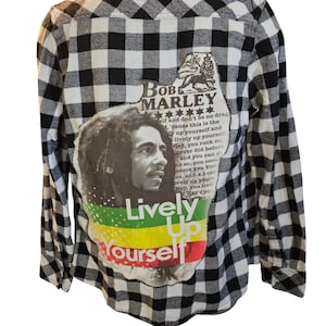 May include: Black and white plaid flannel shirt with a large patch on the back featuring a portrait of Bob Marley with the text "Lively Up Yourself" and the colors of the Jamaican flag.