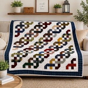 May include: A quilt featuring a white background with diagonal, interlocking ribbon patterns made of various plaid fabrics in shades of red, blue, yellow, green, and brown. The quilt is finished with a dark blue plaid border around the edges.