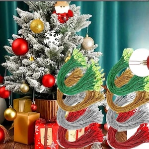 Pode incluir: Uma coleção de cordões metálicos para pendurar ornamentos em verde, dourado, prateado e vermelho. Cada cordão possui um pequeno fecho metálico na extremidade para prender decorações. Os cordões estão agrupados em laços em forma de U ante uma árvore.