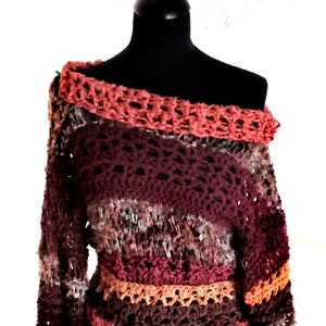 May include: A handmade, off-the-shoulder crochet sweater in shades of burgundy, orange, and brown. The sweater features a textured stitch pattern and a wide, open neckline. The sleeves are long and fitted, with ribbed cuffs. The text "FedRaDD" is in the top left corner.