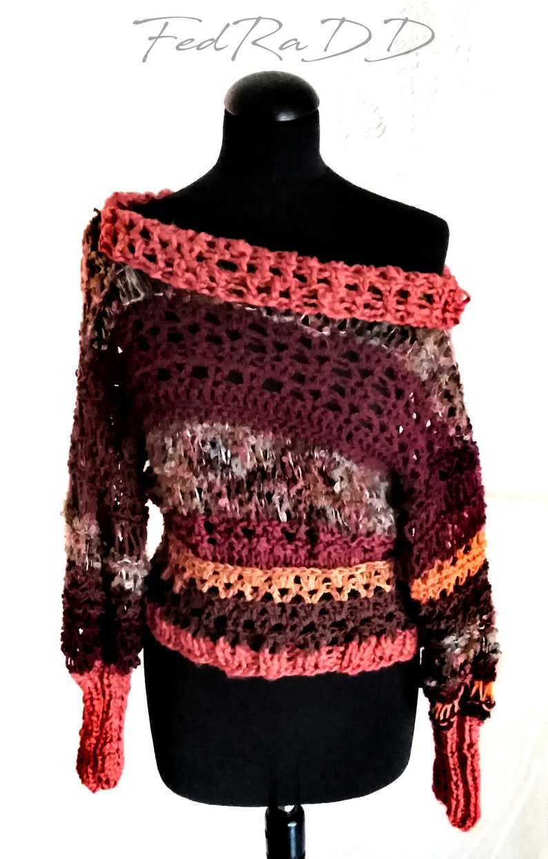 May include: A handmade, off-the-shoulder crochet sweater in shades of burgundy, orange, and brown. The sweater features a textured stitch pattern and a wide, open neckline. The sleeves are long and fitted, with ribbed cuffs. The text "FedRaDD" is in the top left corner.