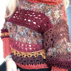 May include: A handmade, open-weave sweater in shades of burgundy, rust, and gold. The sweater features a unique crochet design with a textured, multi-colored yarn. The sleeves and neckline have a ribbed knit detail. A stylish, bohemian-inspired garment.