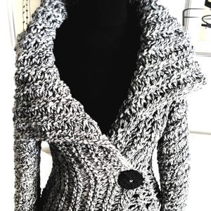 May include: A black and white knitted cardigan with a large collar and a single button closure. The cardigan is made of a chunky yarn and has a relaxed fit.