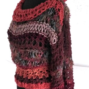 May include: A handmade, multi-colored crochet sweater displayed on a black mannequin. The sweater features a variety of colors, including burgundy, rust, and gray. The neckline and cuffs are a solid rust color. The text "Fed Ra D D" is in the upper left corner.