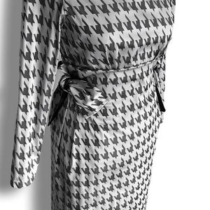May include: A white and black off-the-shoulder dress with a houndstooth pattern. The dress has long sleeves and a tie at the waist.