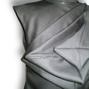 May include: A black sleeveless shirt with a unique folded design. The fabric is folded in a way that creates a series of triangular shapes.
