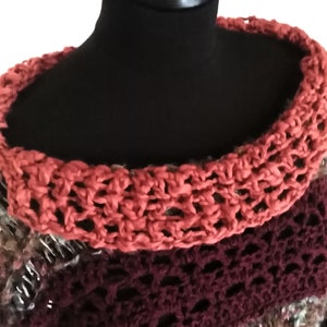 May include: A handmade, multi-colored crochet sweater displayed on a black mannequin. The sweater features a wide, open-weave collar in a coral hue, transitioning to a deep burgundy and then to a mix of brown and other colors. The text "FedRa DD" is in the top left corner.