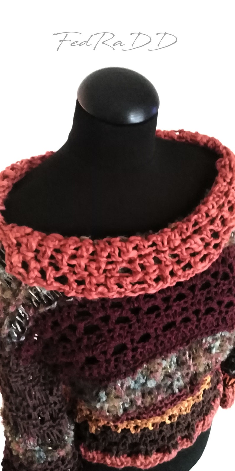 May include: A handmade, multi-colored crochet sweater displayed on a black mannequin. The sweater features a wide, open-weave collar in a coral hue, transitioning to a deep burgundy and then to a mix of brown and other colors. The text "FedRa DD" is in the top left corner.
