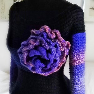 May include: Black knitted top with a large, vibrant, purple and pink crocheted flower detail. The sleeves are blue and purple. The word "fedRADD" is written at the top.