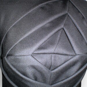 May include: Black sleeveless shirt with a geometric design created by pleats in the fabric.