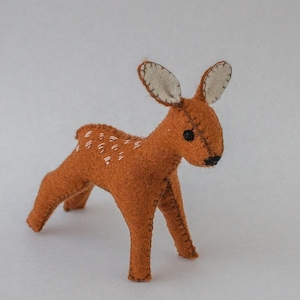 May include: A brown felt deer with white embroidered spots and white felt ears. The deer has black eyes and a black nose.