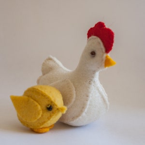 May include: A white felt chicken with a red comb and a yellow felt chick. The chick is smaller than the chicken and is sitting in front of the chicken.