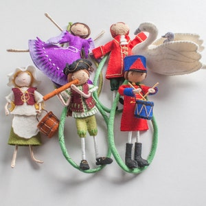 Può includere: Un set di cinque bambole di feltro, ognuna con abiti e accessori unici. Le bambole includono una ballerina, un soldato, un musicista, una ragazza con un vestito e un cigno. Le bambole sono tutte fatte a mano e hanno uno stile fantasioso e vintage.