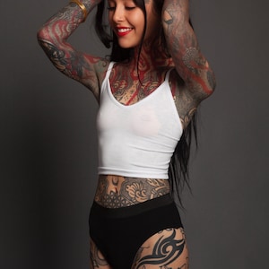 Puede incluir: Un top corto sin mangas de color blanco con escote redondo combinado con ropa interior negra de talle alto. El conjunto presenta un diseño sencillo con una silueta ajustada, líneas limpias y un acabado liso, centrado en la confección textil.