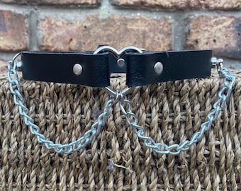 May include: A black leather choker with a silver heart charm and two silver chains attached.