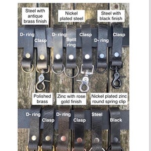 May include: A collection of black buffalo leather belt loops featuring various metal hardware attachments including D-rings, clasps, split rings, and spring clips. The hardware finishes include antique brass, nickel, black, polished brass, and rose gold.