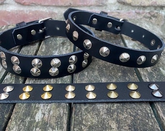 May include: Two black leather collars featuring silver-toned metal cone studs arranged in double rows, accompanied by a flat black leather strip displaying a variety of metallic cone studs in silver, gold, and gunmetal finishes with buckle closures.