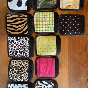 May include: A collection of rectangular fabric patches with hook and loop fasteners. The patches feature various patterns, including cow print, camouflage, zebra stripes, plaid, polka dots, and leopard print. The patches are arranged on a wooden surface.